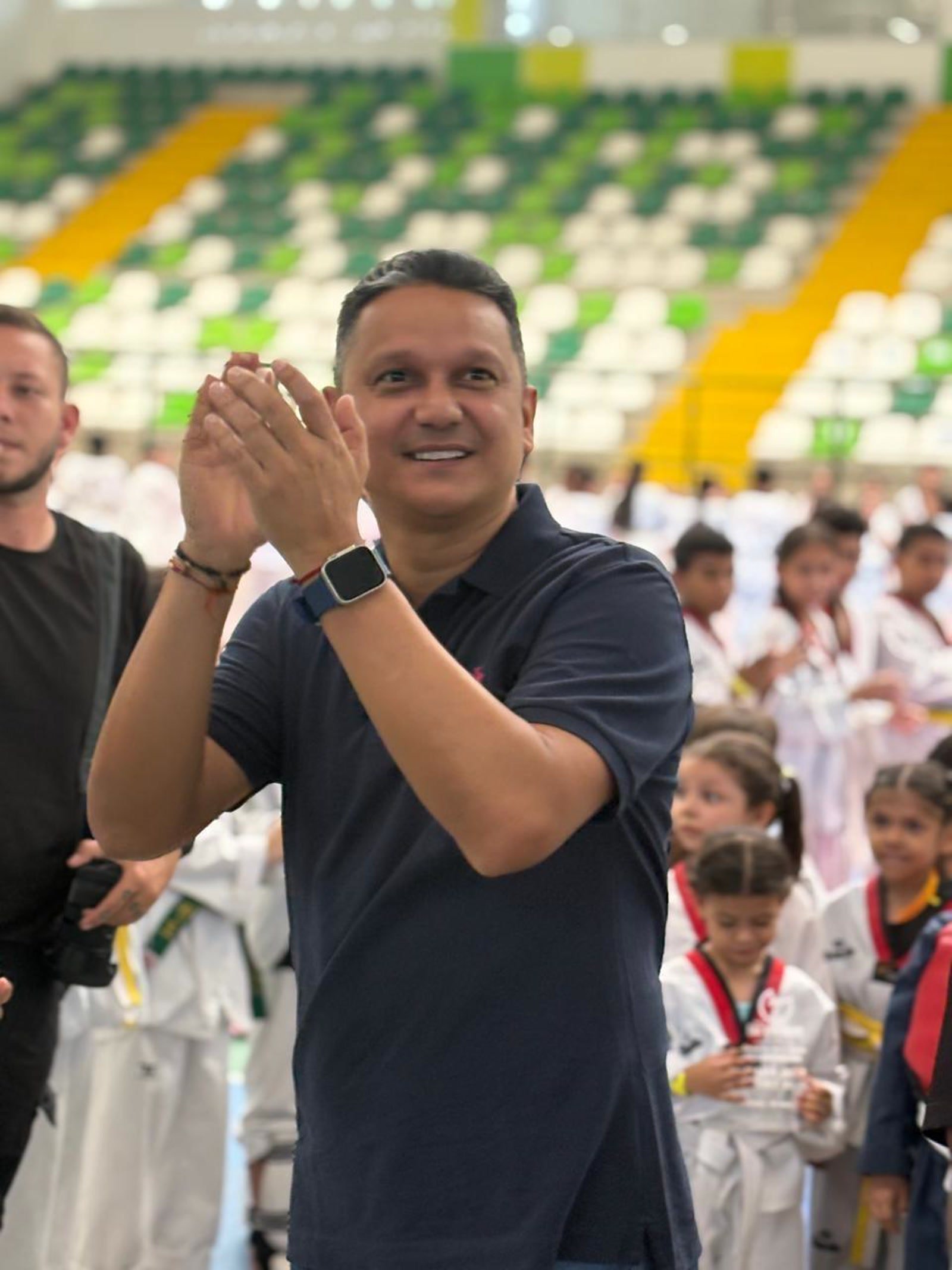 Elmer Jiménez aplaudiendo en un coliseo durante un evento de taekwondo infantil